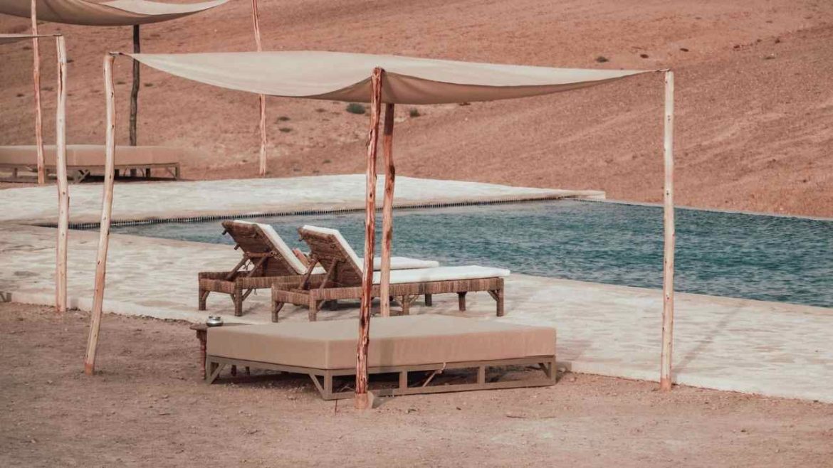Luxury desert glamping pool area with wicker lounge chairs and shade canopies in arid landscape