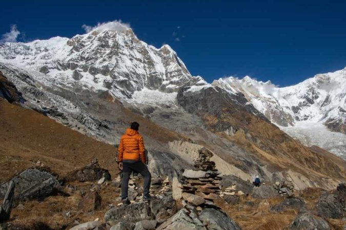 Trekker in orange jacket admiring snow-capped mountains along Nepal's Annapurna Circuit trail