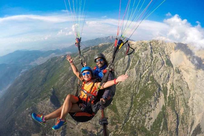 Tandem paragliding for beginners with instructor and student flying over mountainous landscape