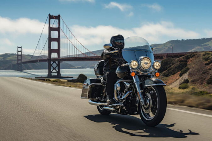 A rider cruising on a large touring motorcycle along a coastal highway with the Golden Gate Bridge of San Francisco in the background during a motorbike tours usa