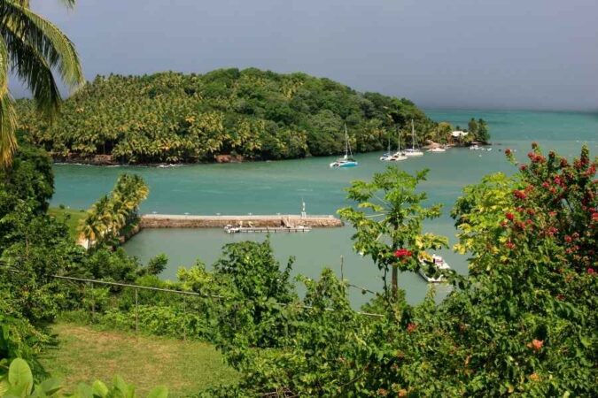 A serene tropical bay featuring a lush green island surrounded by calm turquoise water and several moored sailboats.